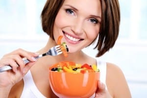 The beautiful smiling young woman with a plate of fresh vegetable salad in hands